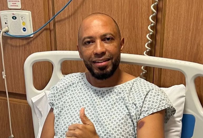 O cantor Salgadinho sorrindo, posando em uma foto, com a informação de que ele passou por uma cirurgia bem-sucedida.