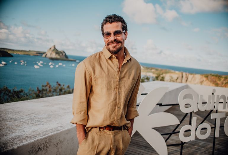 Thiago Martins sorrindo com um cenário de show ao fundo, celebrando o lançamento de seu projeto musical.